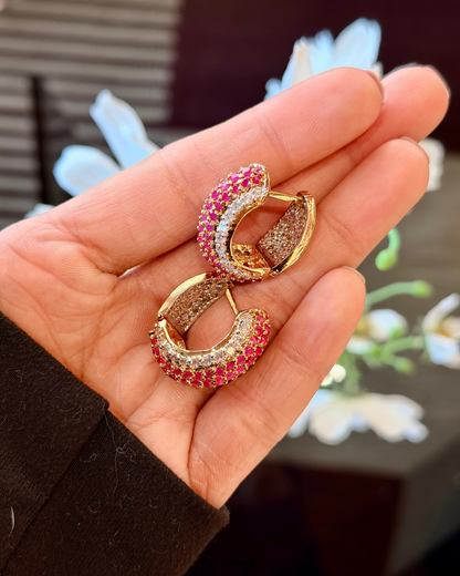 Gold and pink earrings held in a hand with a blurred background