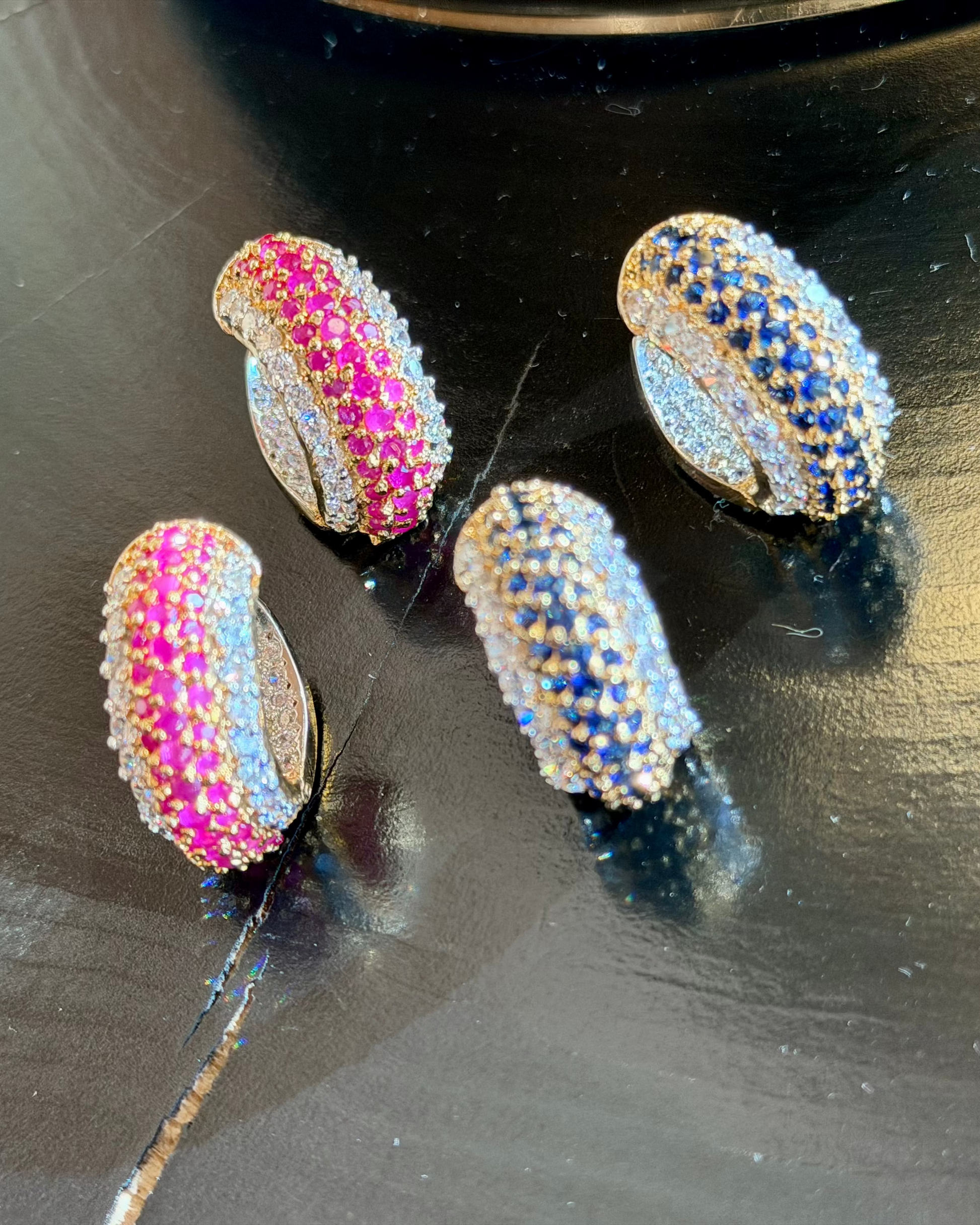 Four multicolored gemstone earrings on a reflective surface