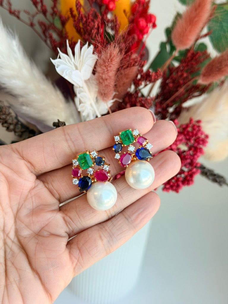 Multicolored gemstone earrings with pearl center held in a hand against a floral background