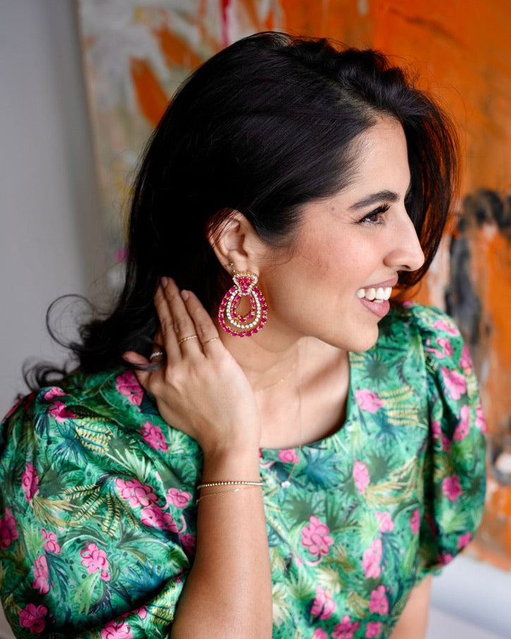 Woman wearing a green floral dress with pink flowers, smiling indoors.